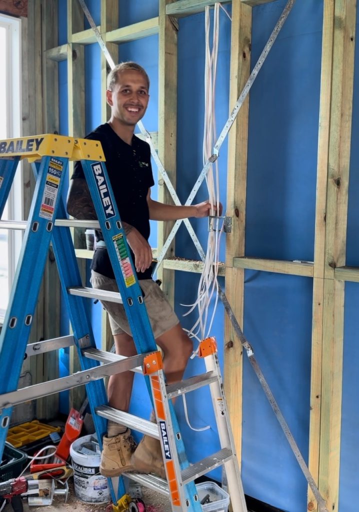 A team member working on a new residential home standing on a ladder holding cables. A day on site with our electrician Newcastle