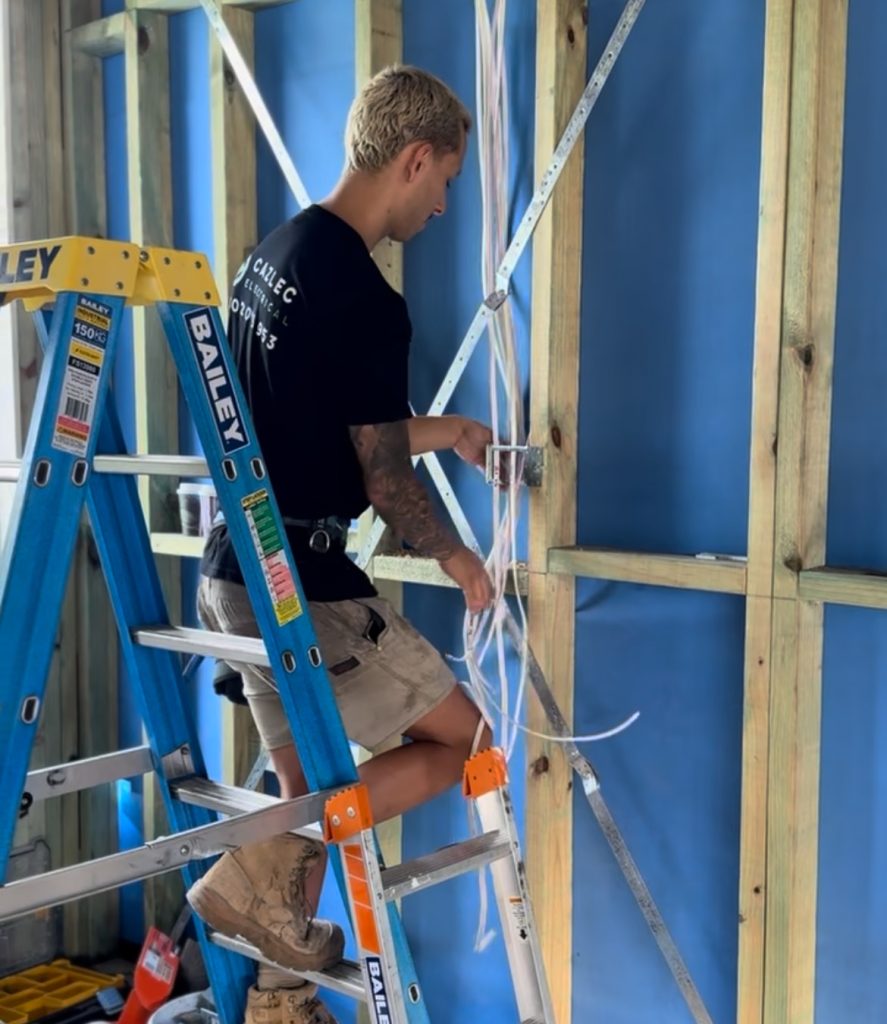 A team member working on a new residential home standing on a ladder holding cables facing away from camera. Showing our Newcastle Electricians at work